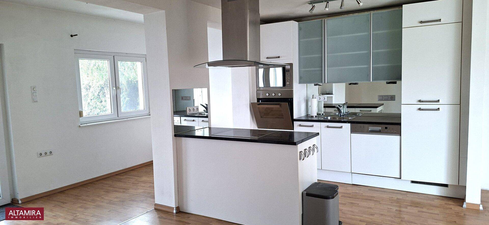 Moderne offene Küche mit weißen Schränken, Kochinsel und Holzboden, hell durch ein Fenster.