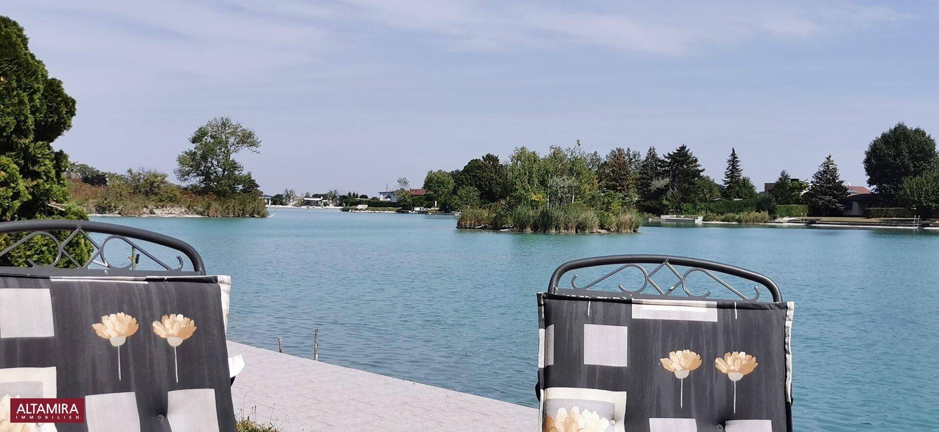 Entspannter Blick auf den See von einer Terrasse mit bequemen Gartenstühlen.