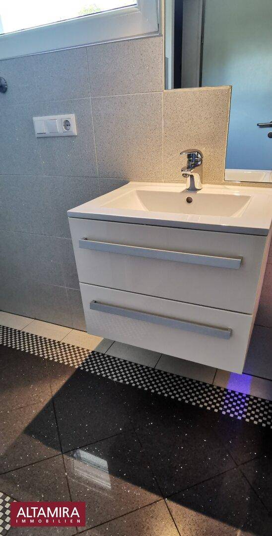 Einzelwaschbecken mit Unterschrank in einem modern gefliesten Badezimmer mit Fenster.