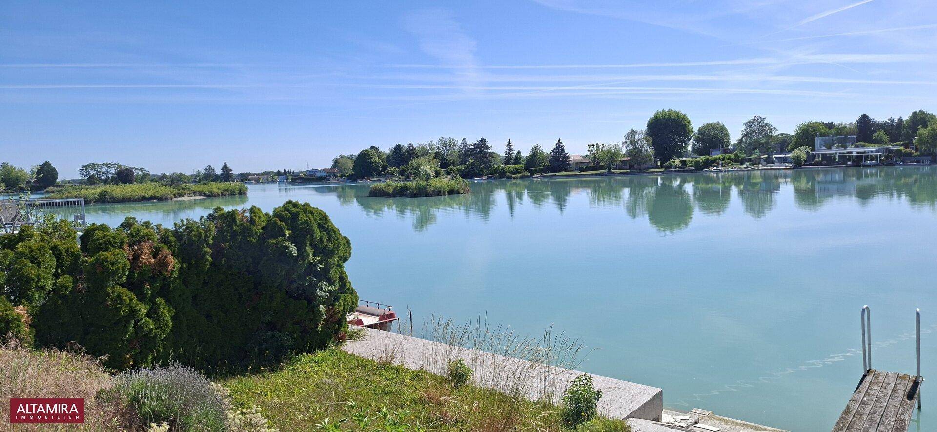 Weitläufiger Blick auf einen ruhigen See mit grünen Ufern und klarem, blauem Himmel.