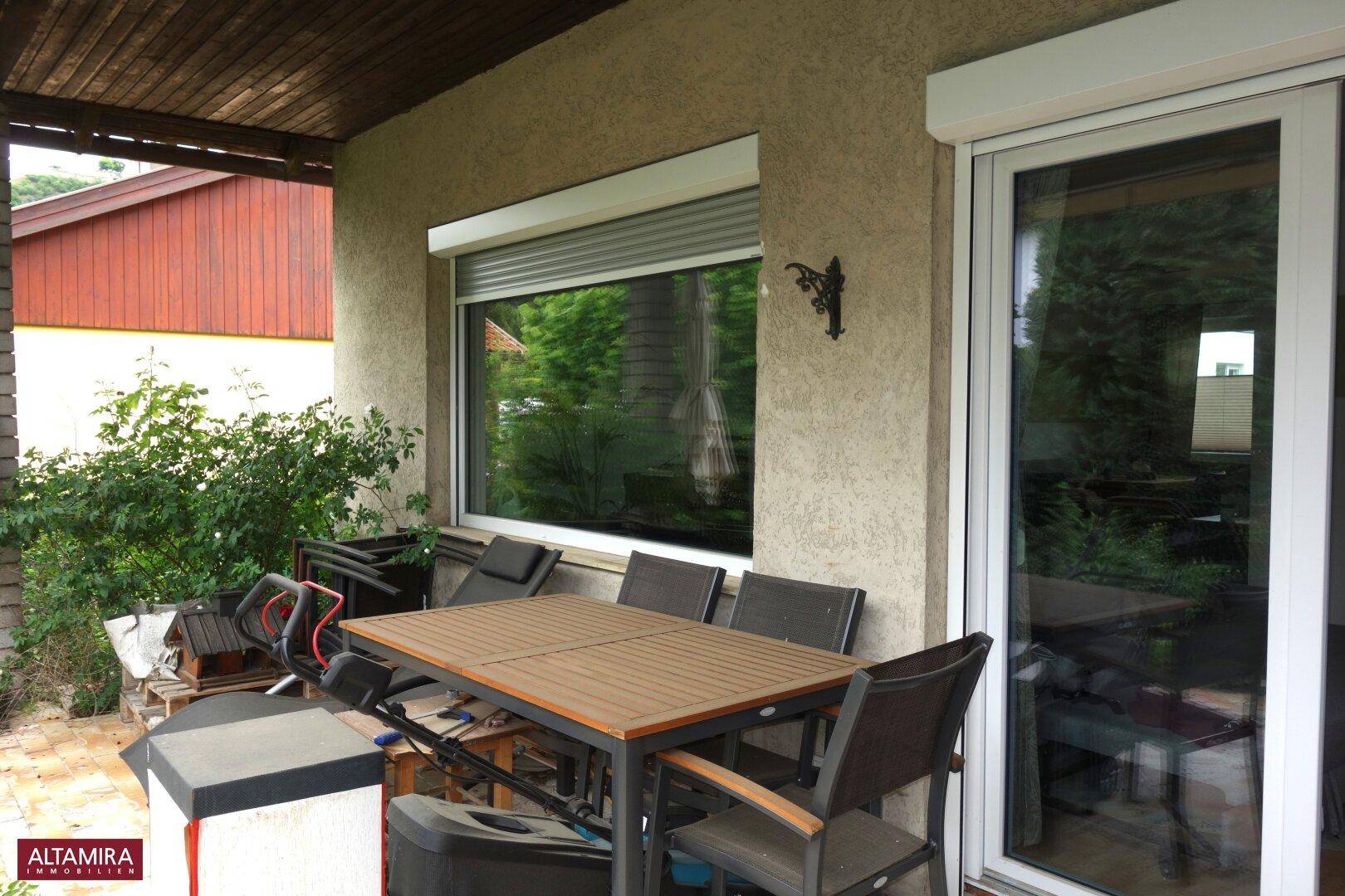 Gemütliche überdachte Terrasse mit Esstisch und Stühlen, ideal für Mahlzeiten im Freien.
