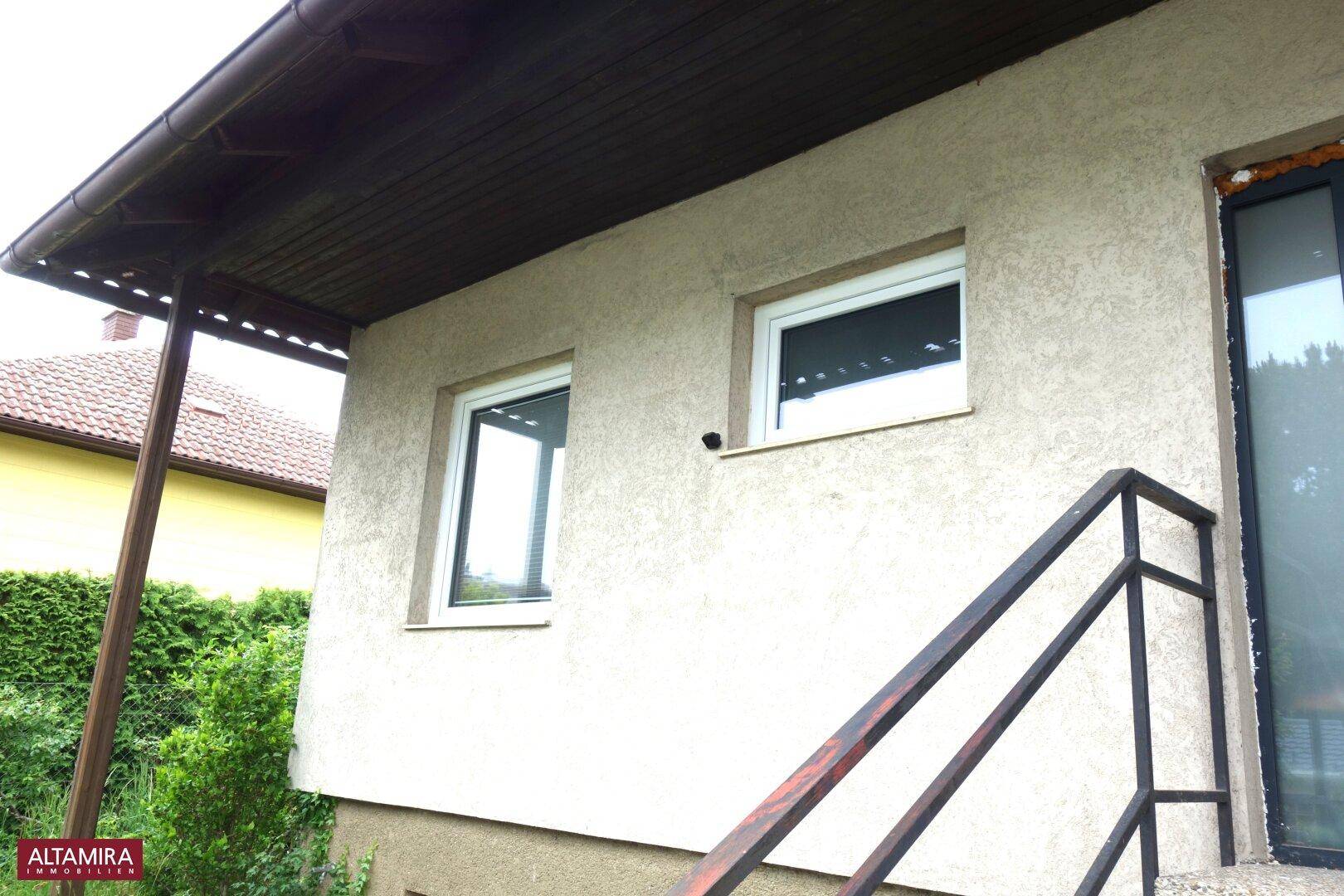 Seitenansicht des Hauses mit Fenstern, Treppe und überdachtem Eingangsbereich.