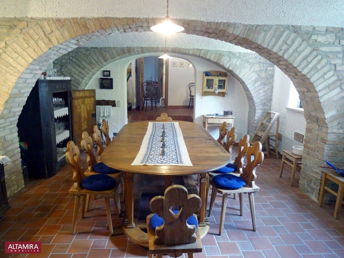 Rustikaler Essbereich mit Ziegelbögen, Terrakottafliesen und einem großen Holztisch.