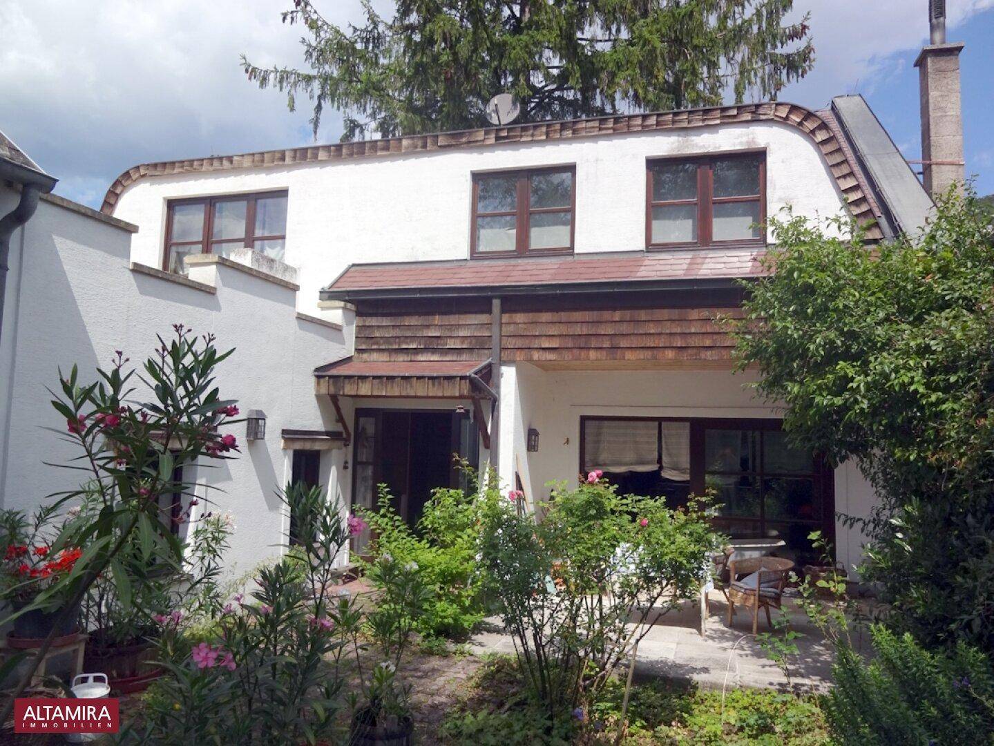 Rückansicht des Hauses mit einer kleinen Terrasse und üppiger Bepflanzung im Garten.