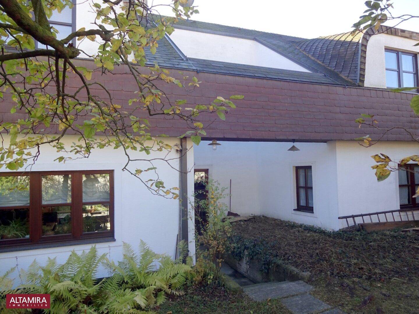 Ansicht der Hausrückseite mit Rampe und Fenstern, umgeben von Herbstlaub.