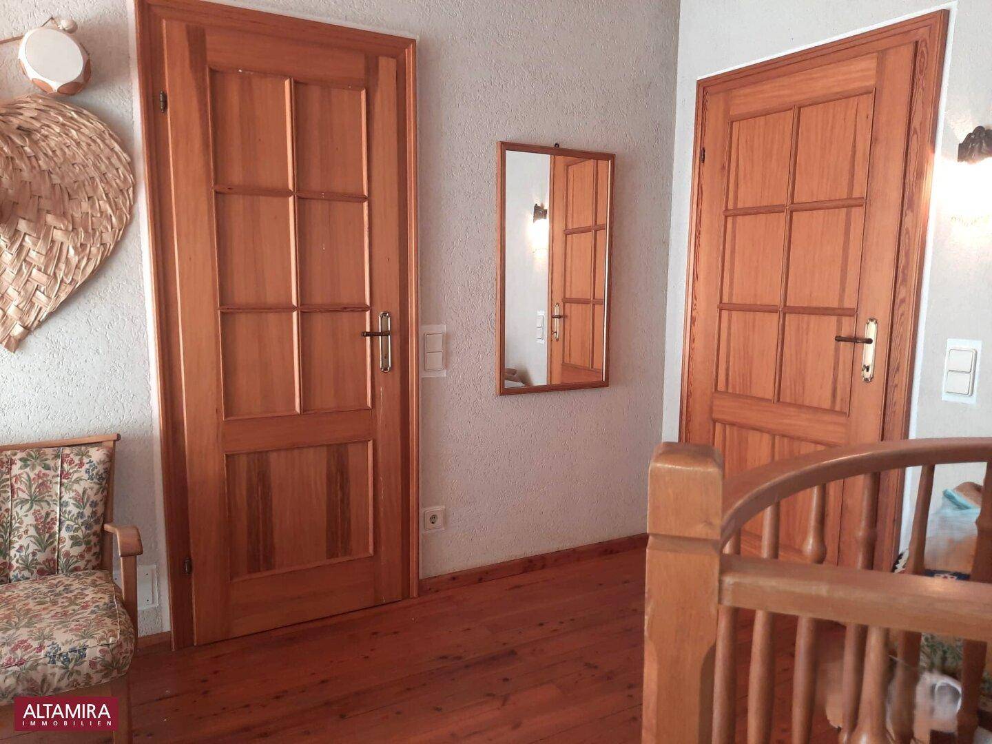 Flur mit zwei Holztüren, einem kleinen Spiegel und Holzdielenboden.