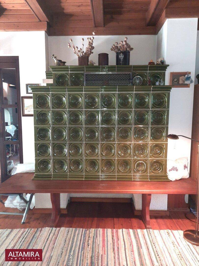 Detailansicht eines großen, grünen Kachelofens als zentrales Heizelement im Wohnzimmer.