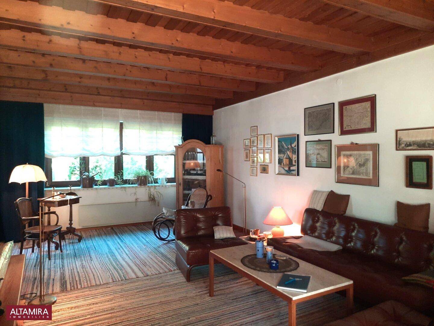 Geräumiges Wohnzimmer mit Holzbalkendecke, Ledermöbeln und großen Fenstern.