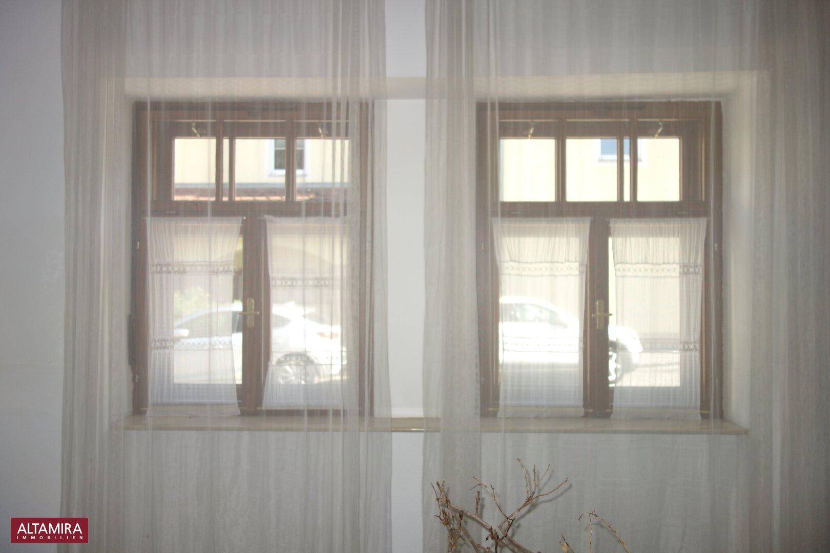Zwei Fenster mit Gardinen, die Tageslicht in den Raum lassen.
