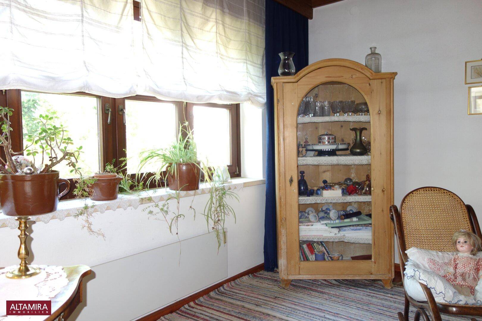 Fensterbereich im Wohnzimmer mit Pflanzen, einem Holzschrank und Blick ins Grüne.