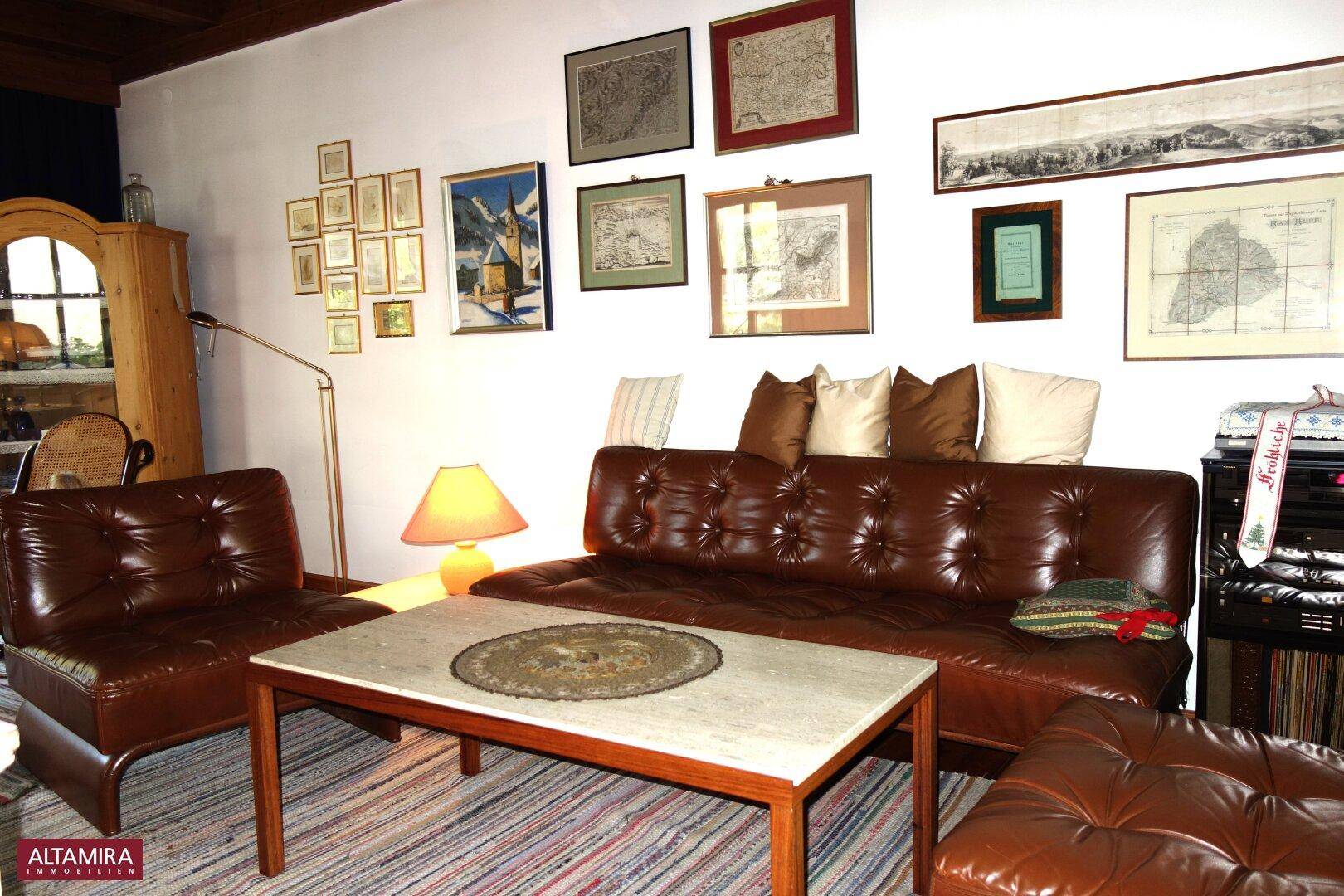 Gemütliches Wohnzimmer mit Ledersofa, Couchtisch und vielen gerahmten Bildern an der Wand.