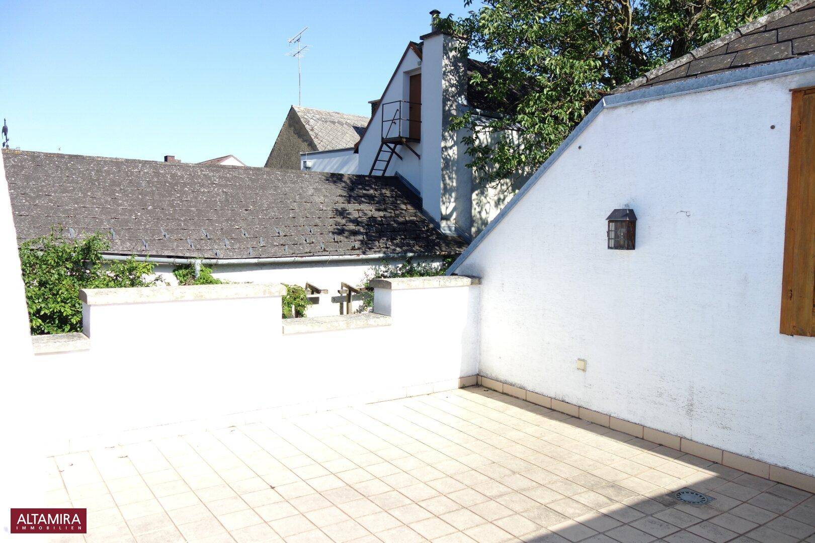 Eine sonnige, geflieste Dachterrasse mit Blick auf die umliegenden Dächer.