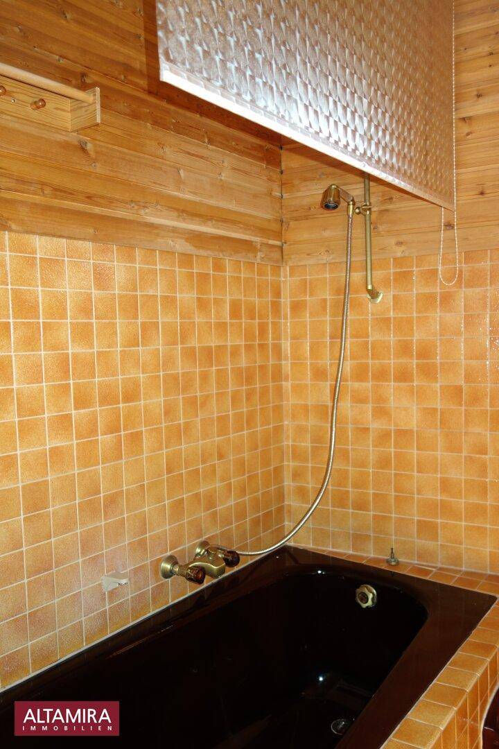 Badezimmer mit brauner Badewanne, Duscharmatur und orangefarbenen Wandfliesen.