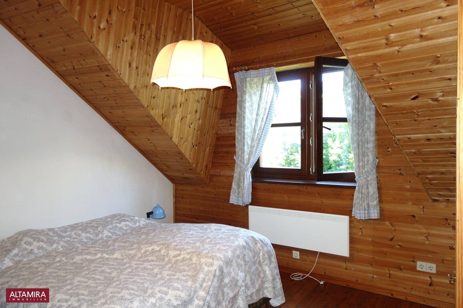Helles Schlafzimmer im Dachgeschoss mit Holzwänden, Fenster und Heizkörper.