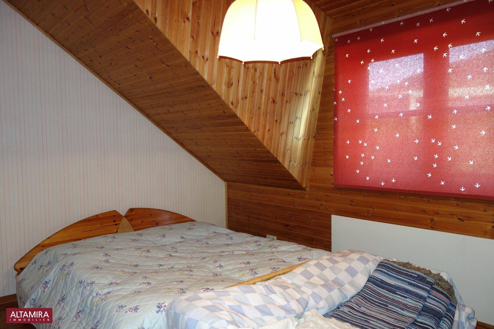 Schlafzimmer im Dachgeschoss mit Holzwänden, schräger Decke und einem Doppelbett.