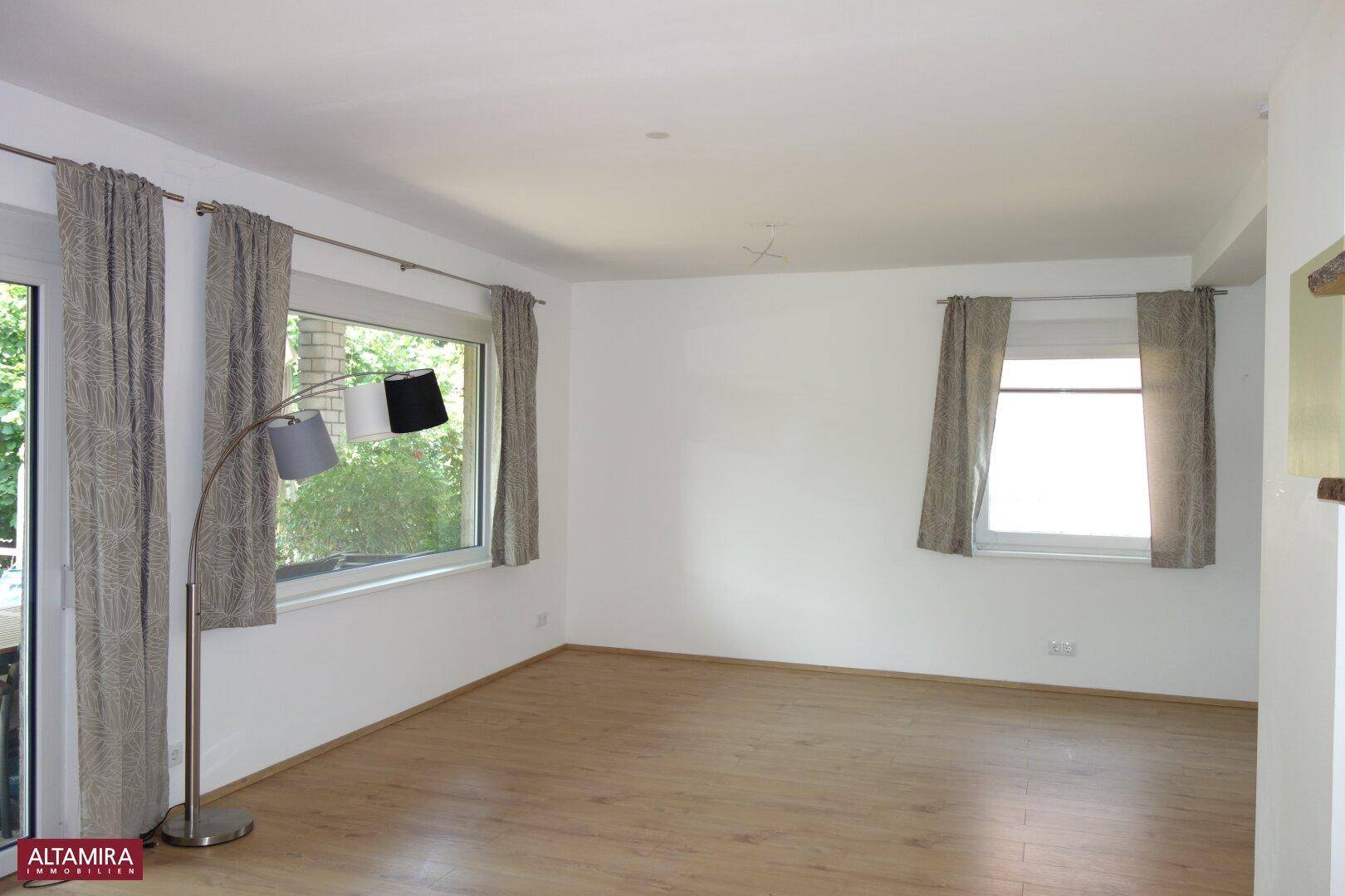Lichtdurchflutetes Wohnzimmer mit großen Fenstern und Terrassenzugang, ideal für Entspannung.