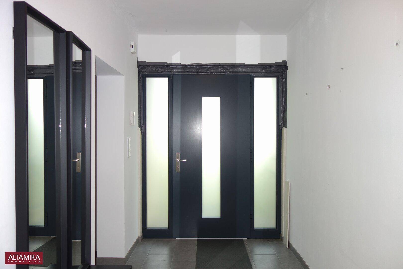 Eingangsbereich mit moderner dunkler Haustür, seitlichen Glaselementen und Fliesenboden.