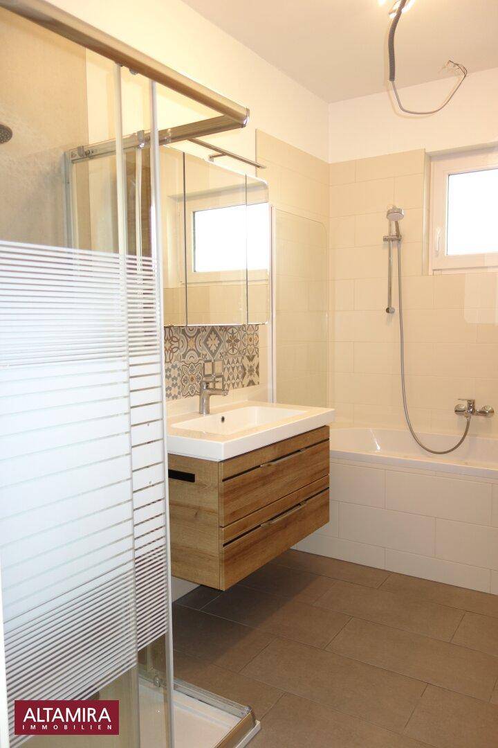 Helles Badezimmer mit Dusche, Badewanne, Einzelwaschbecken und Fenster für Tageslicht.