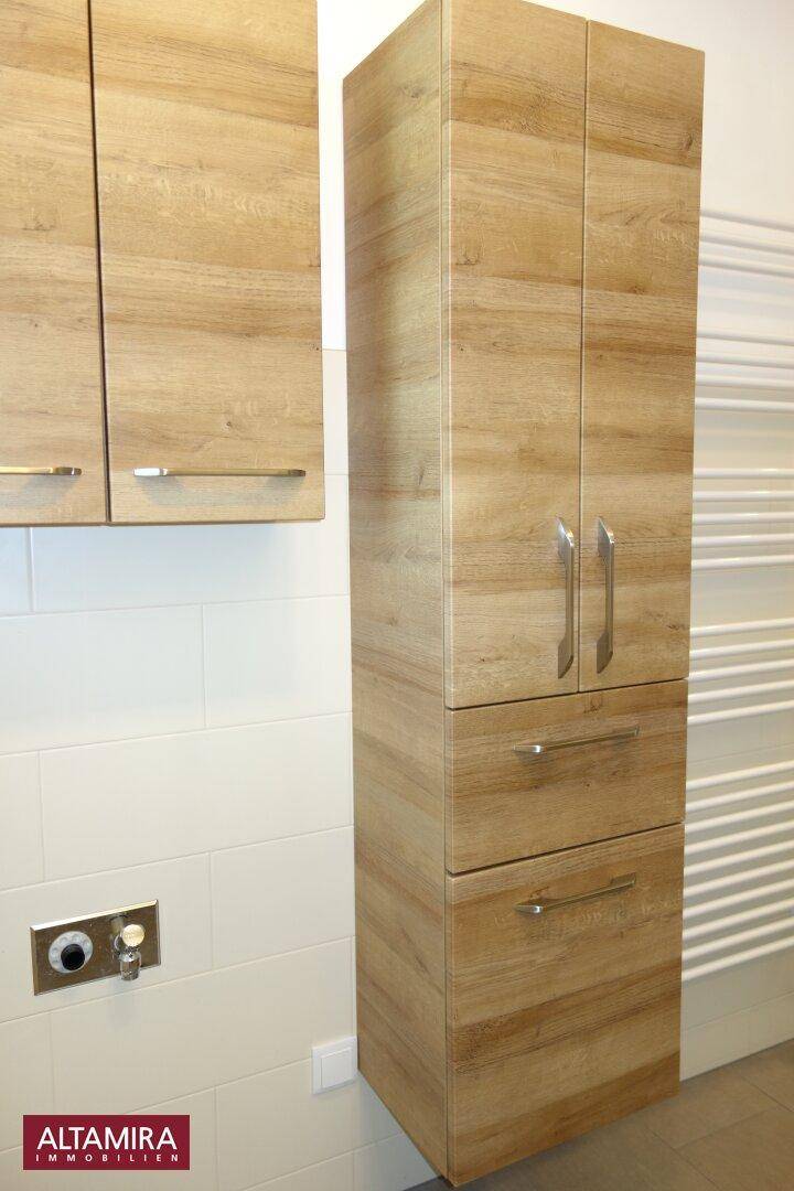 Hoher Holzschrank im Badezimmer neben einem beheizten Handtuchhalter und weißen Fliesen.