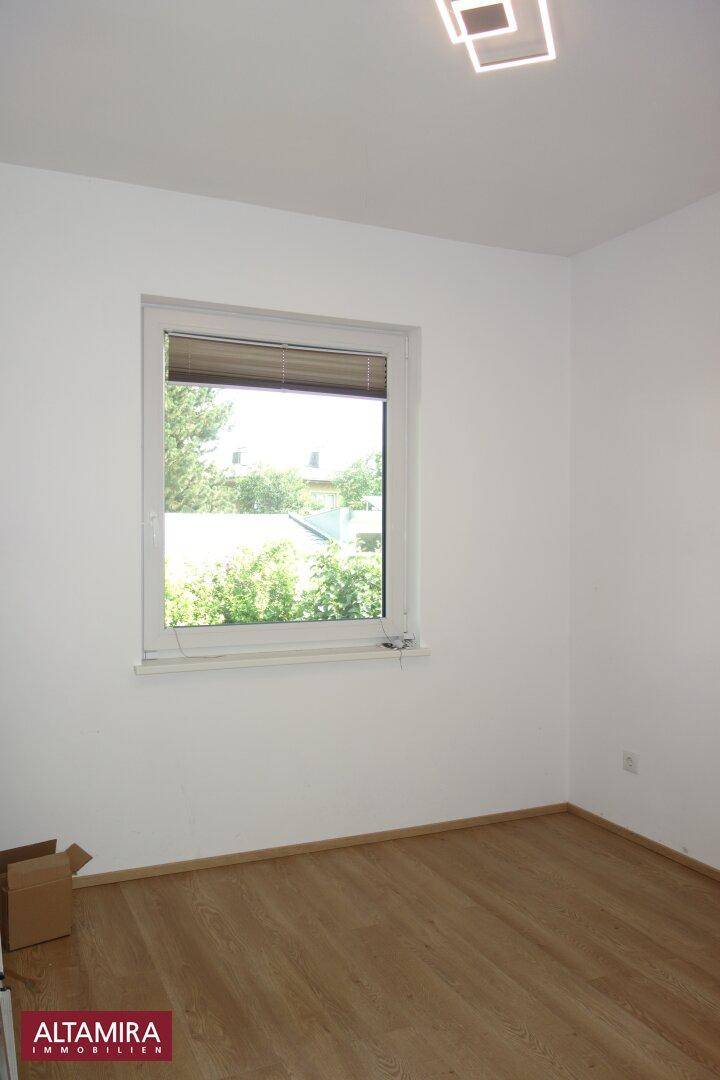 Freundliches Schlafzimmer mit Laminatboden und großem Fenster für viel Tageslicht.