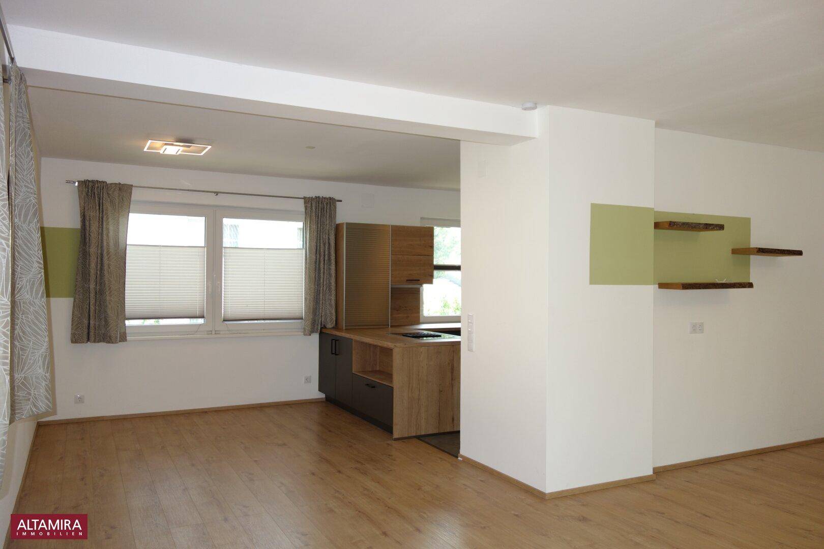 Offener Wohn- und Essbereich mit integrierter Küche und hellem Laminatboden.