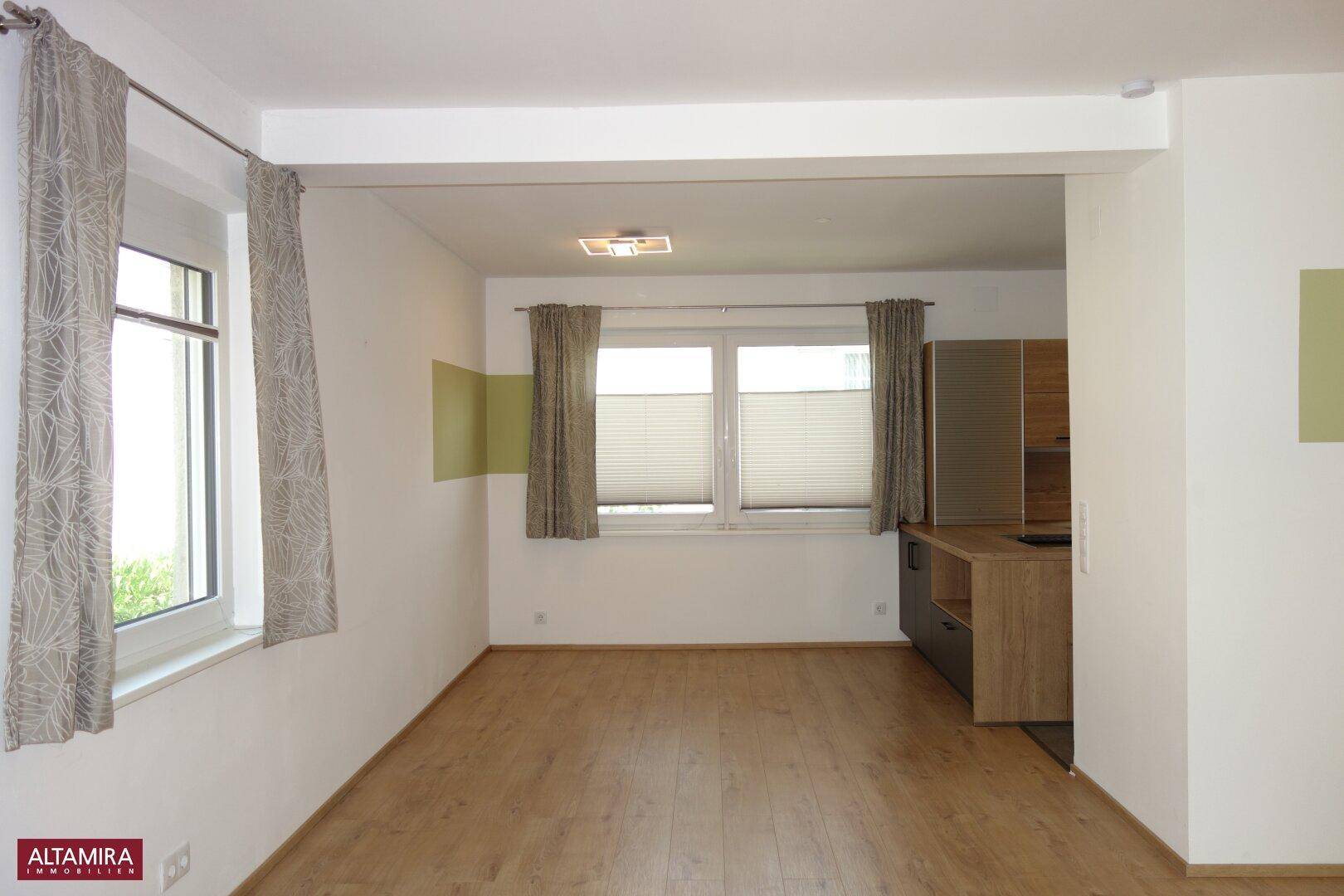 Geräumiger offener Wohnbereich mit Laminatboden und viel Tageslicht durch große Fenster.