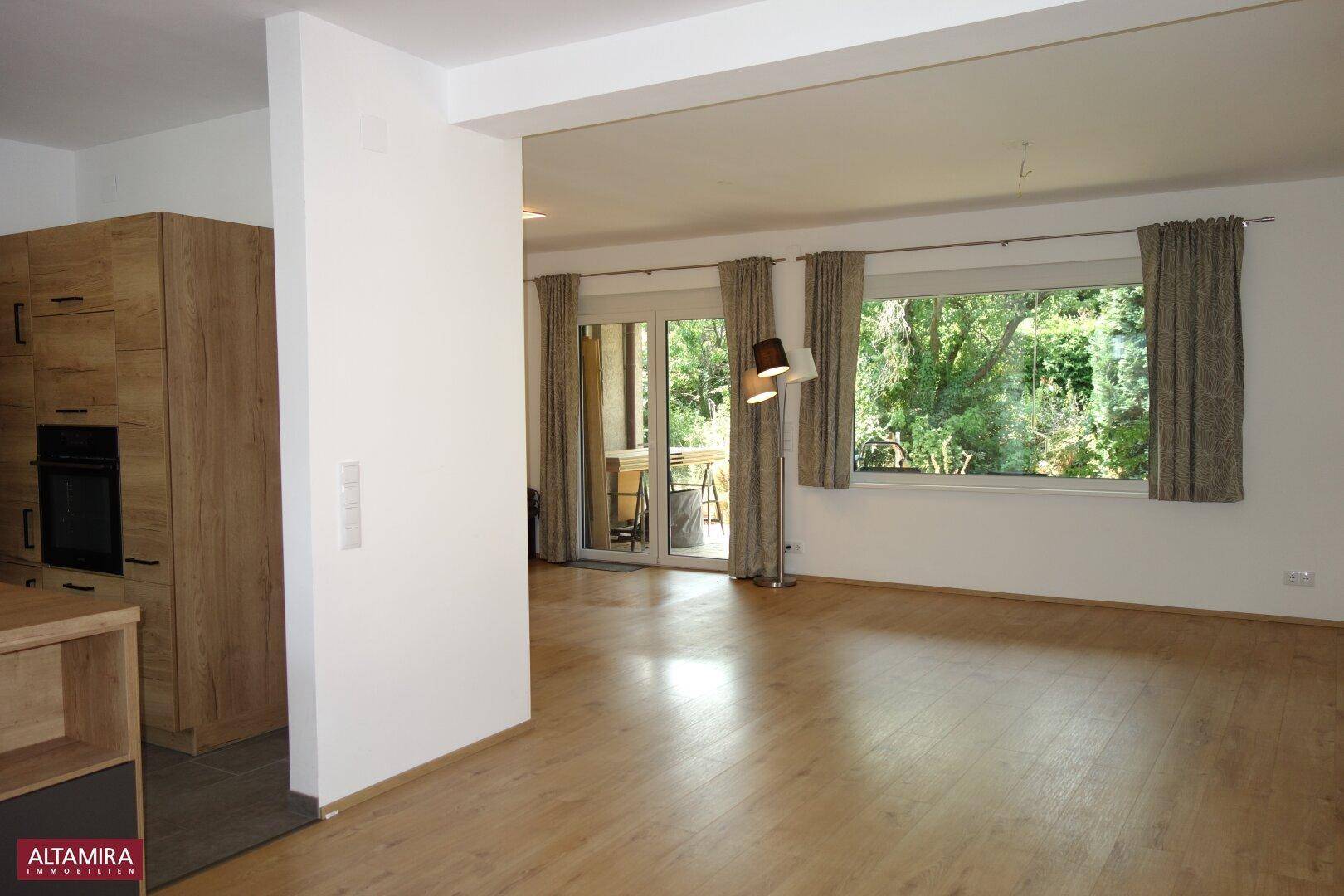 Offener Wohn-Essbereich mit integrierter Küche, Terrassenzugang und Blick auf die Natur.