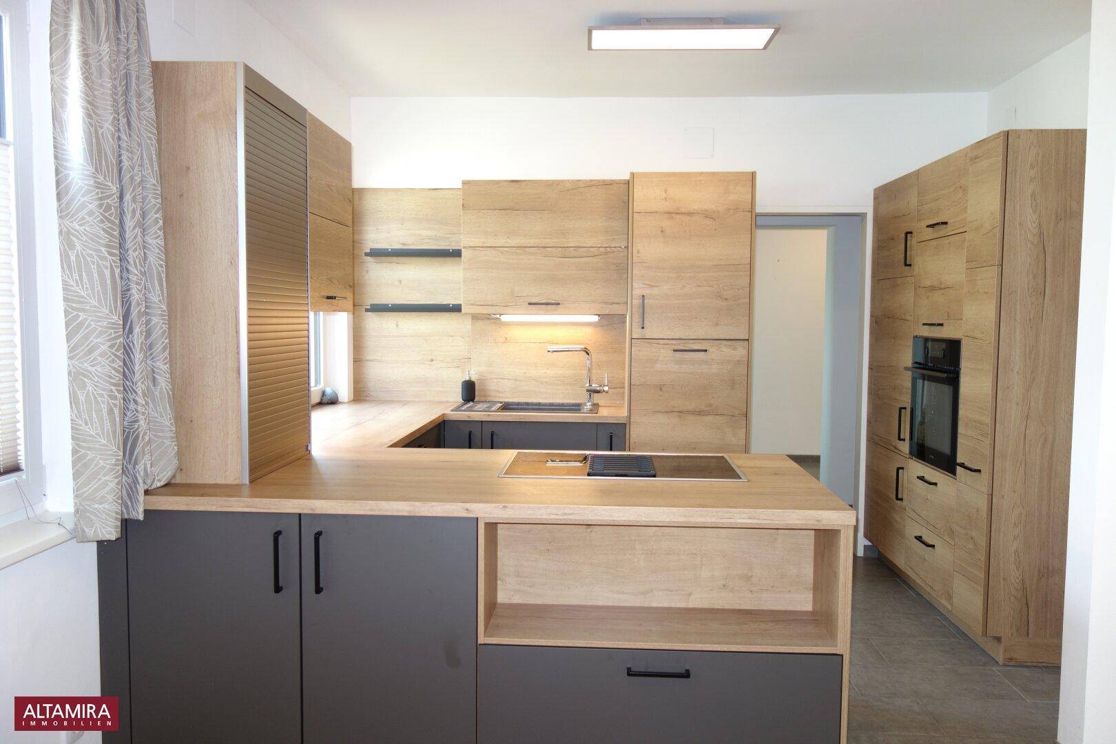 Gut ausgestattete Küche mit integriertem Backofen und modernen Holzoptik-Fronten.
