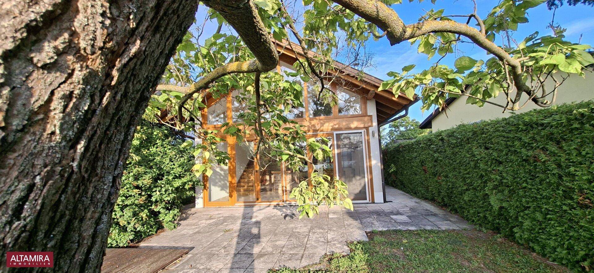 Außenansicht des Hauses mit großen Glasfronten und einer einladenden gepflasterten Terrasse.