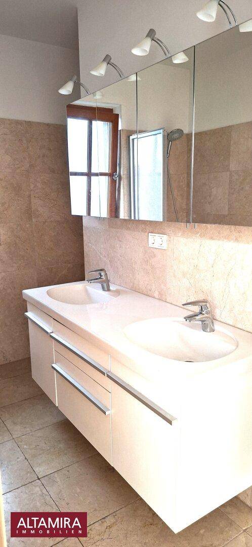 Modernes Badezimmer mit Doppelwaschbecken, großem Spiegel und hellen Fliesen.