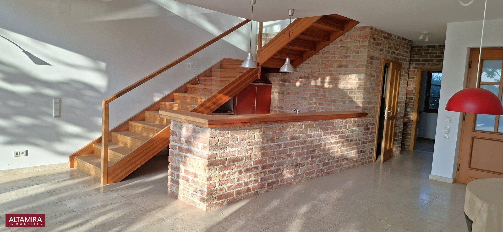 Geräumiger Wohnbereich mit markanter Holztreppe und rustikaler Ziegelbar.