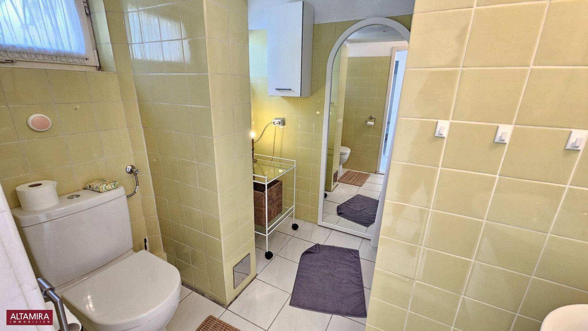 Badezimmer mit gelben Fliesen, Toilette und einem großen Spiegel, der den Raum optisch erweitert.