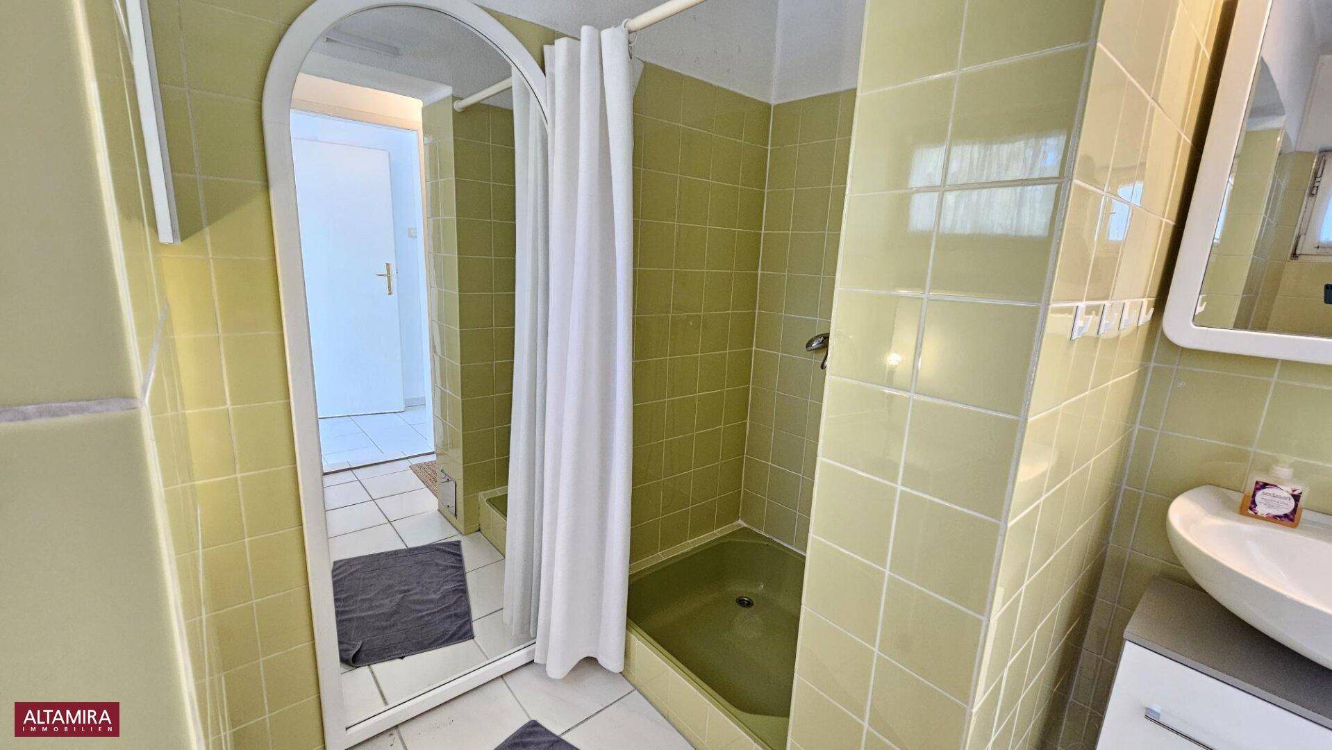 Badezimmer mit gelben Fliesen, Duschbereich und einem Waschbecken mit Spiegel.
