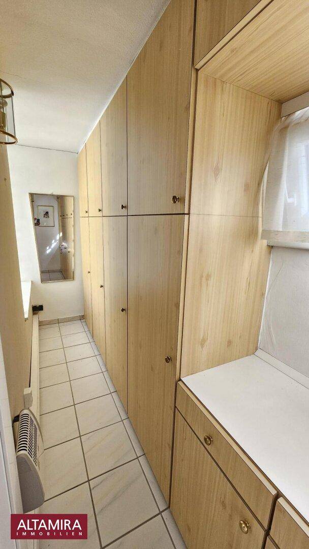Schmaler Flur mit Einbauschränken aus hellem Holz und Fliesenboden.