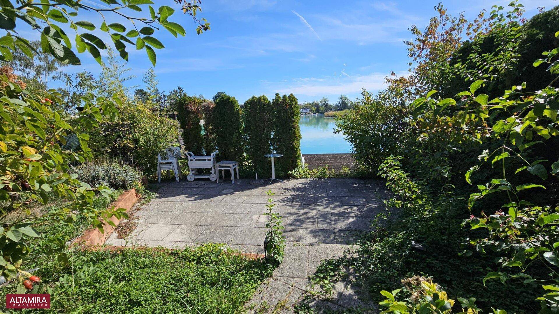 Sonniger Terrassenbereich mit Sitzgelegenheiten und freiem Blick auf den See.