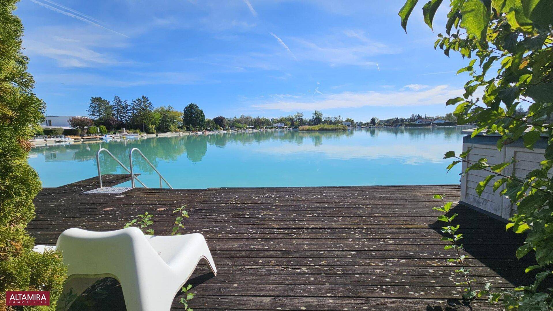 Geräumige Holzterrasse am See mit Liegestuhl und weitem Blick über das Wasser.
