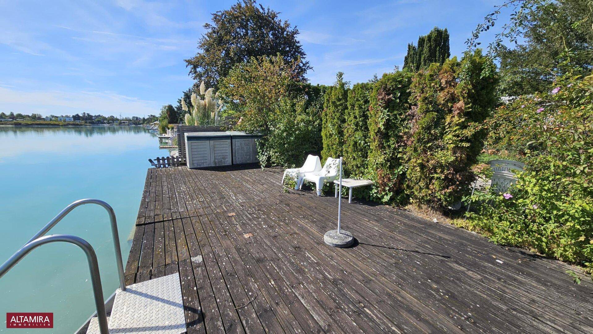 Holzterrasse am Seeufer mit Badeleiter und Blick auf die umliegende Natur.