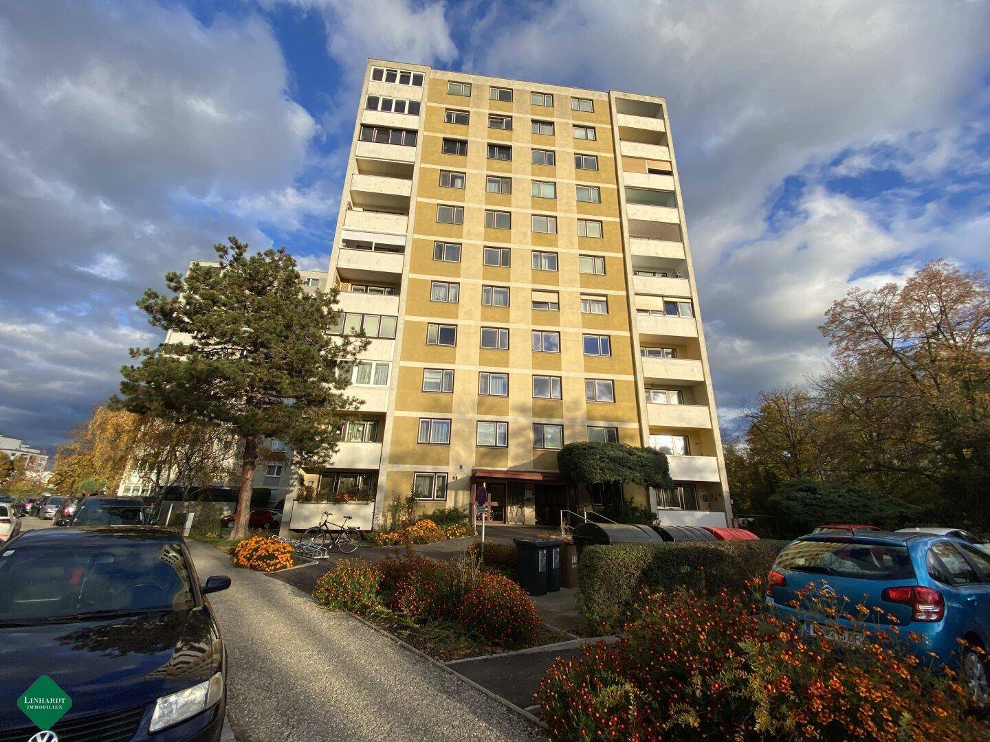 Hohes Mehrfamilienhaus mit vielen Balkonen und gelber Fassade unter bewölktem Himmel.