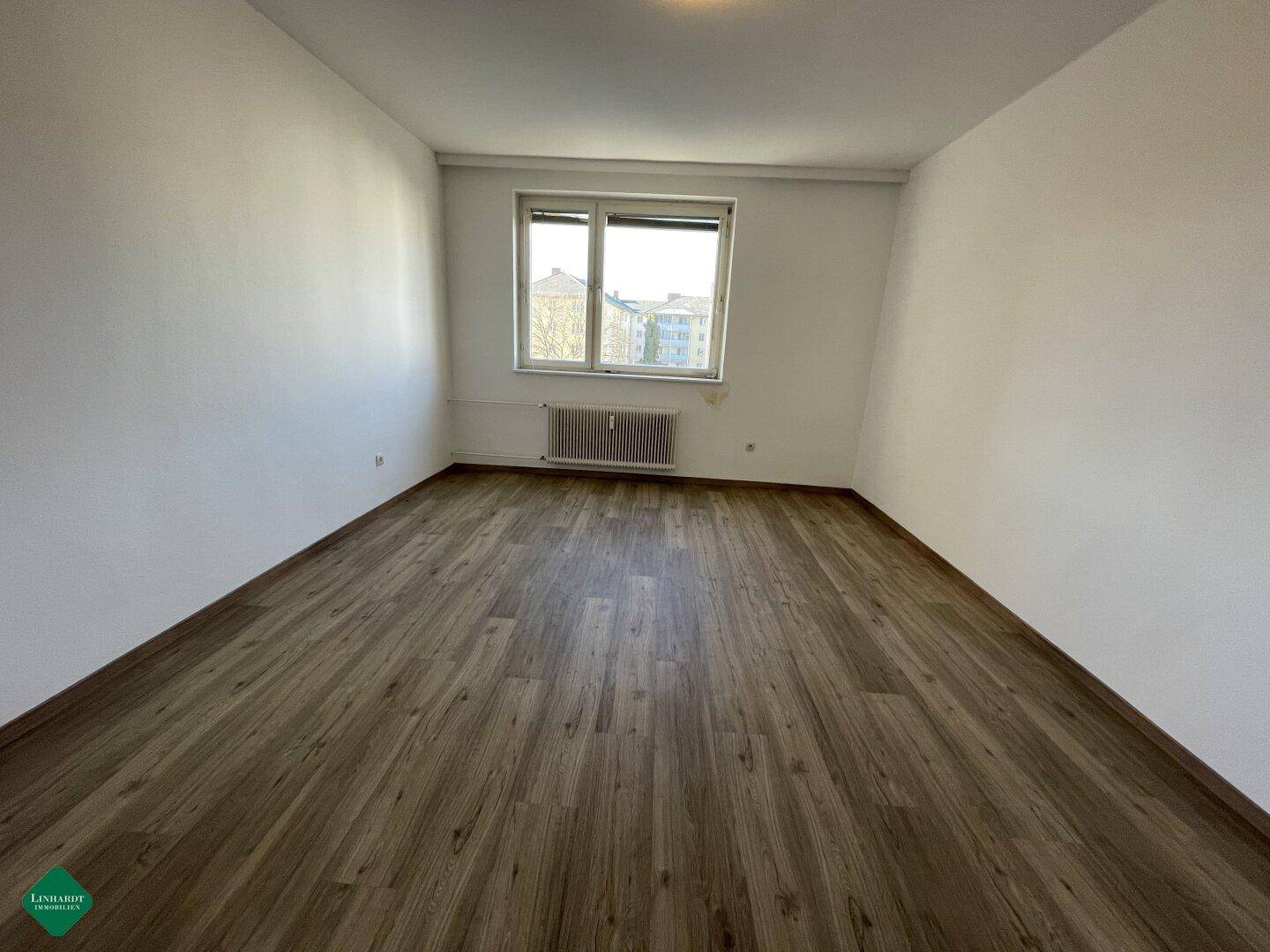 Geräumiges, helles Zimmer mit Laminatboden und einem großen Fenster.