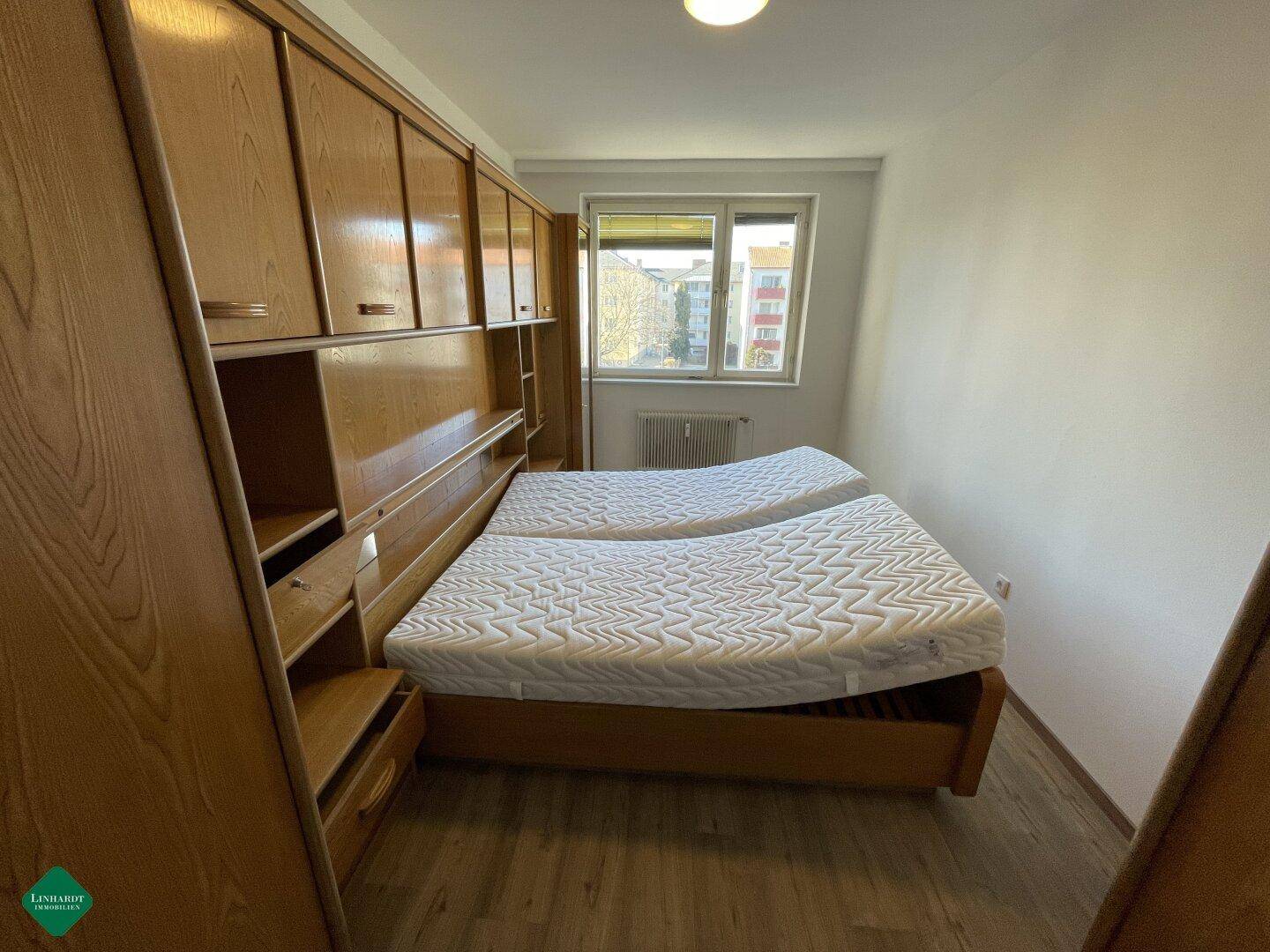 Schlafzimmer mit zwei Betten, Einbauschränken und Fensterblick nach draußen.