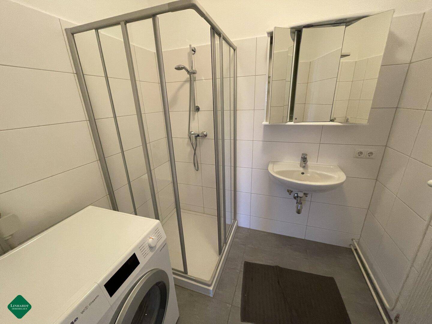 Modernes Badezimmer mit Dusche, Waschbecken, Spiegelschrank und Waschmaschine.