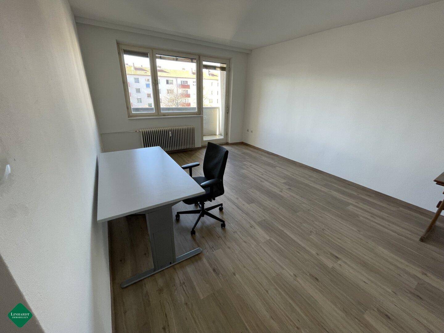 Helles Zimmer mit Laminatboden, großem Fenster und einem Schreibtisch.