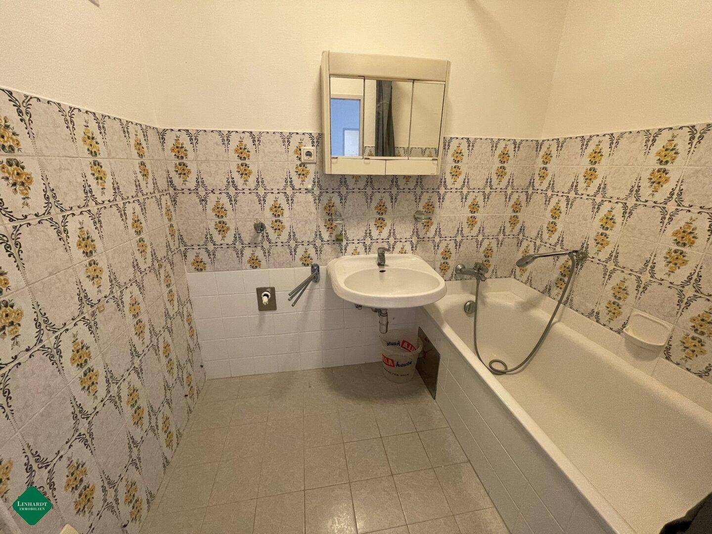 Badezimmer mit Badewanne, Waschbecken und gemusterten Fliesen an den Wänden.