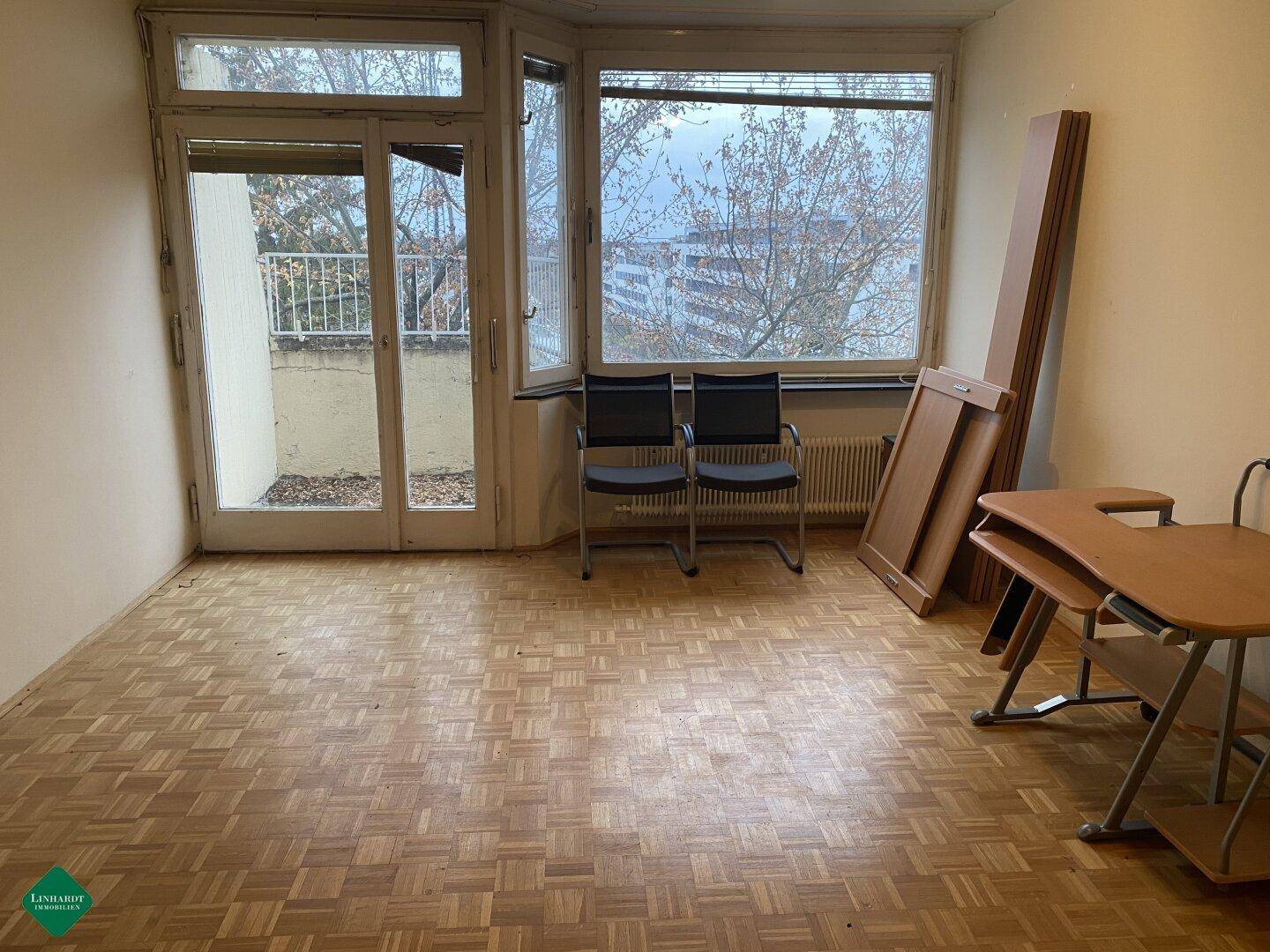 Geräumiges Wohnzimmer mit Parkettboden und Zugang zu einem Balkon durch große Fenster.