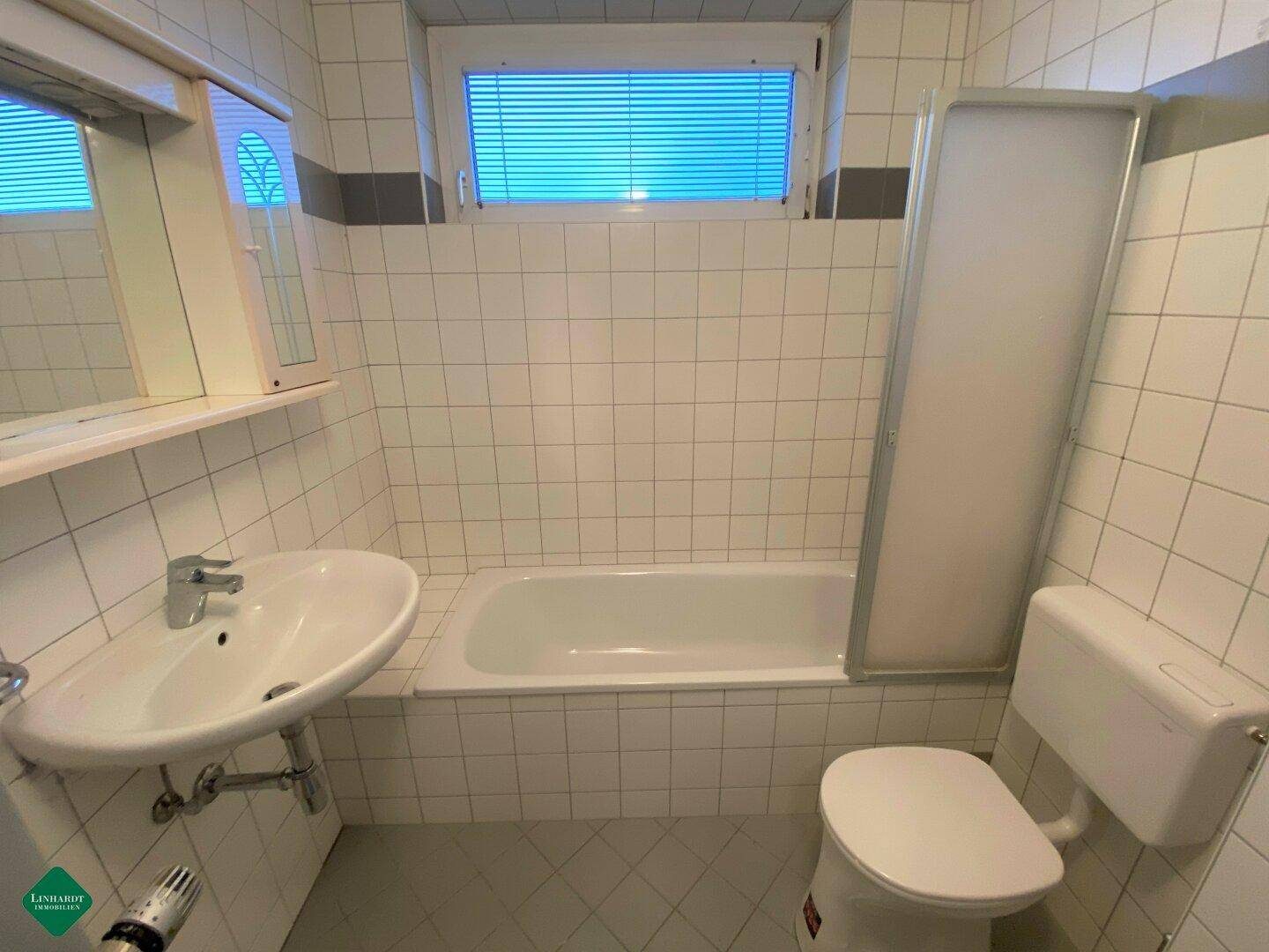 Gefliestes Badezimmer mit Badewanne, Duschabtrennung, Waschbecken und einem Fenster.