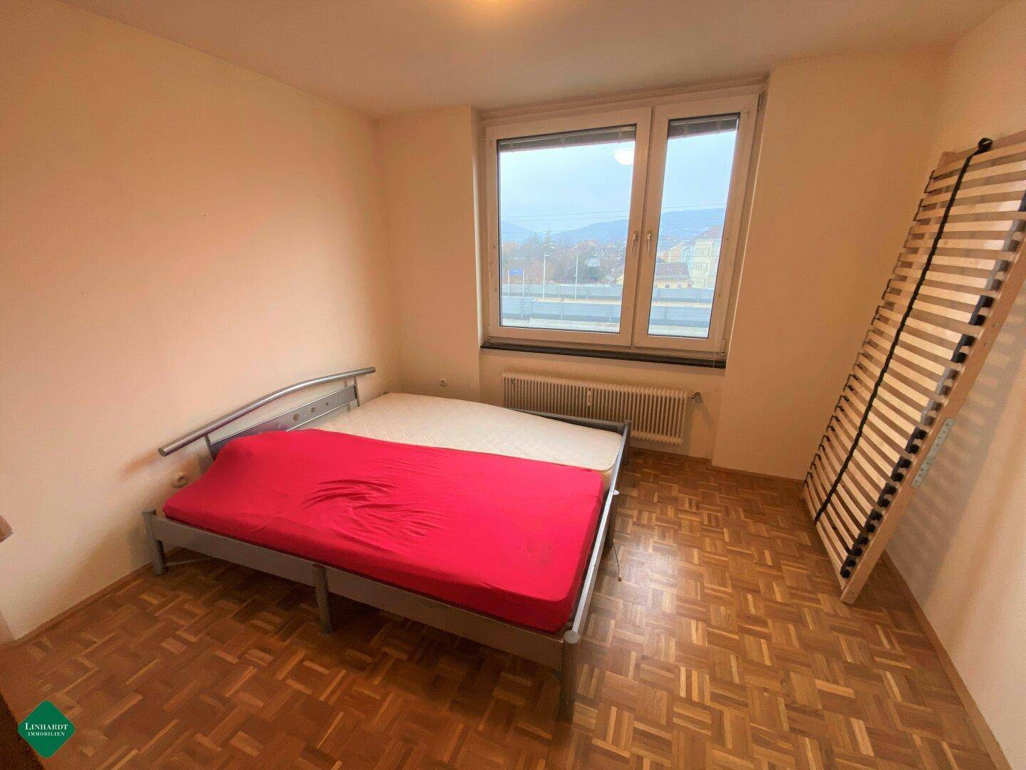 Schlafzimmer mit Parkettboden, großem Fenster und ausreichend Platz für ein Doppelbett.