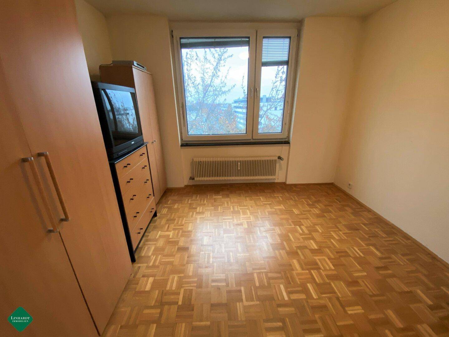 Gemütliches Schlafzimmer mit Parkettboden, Kleiderschrank und Fenster für natürliches Licht.