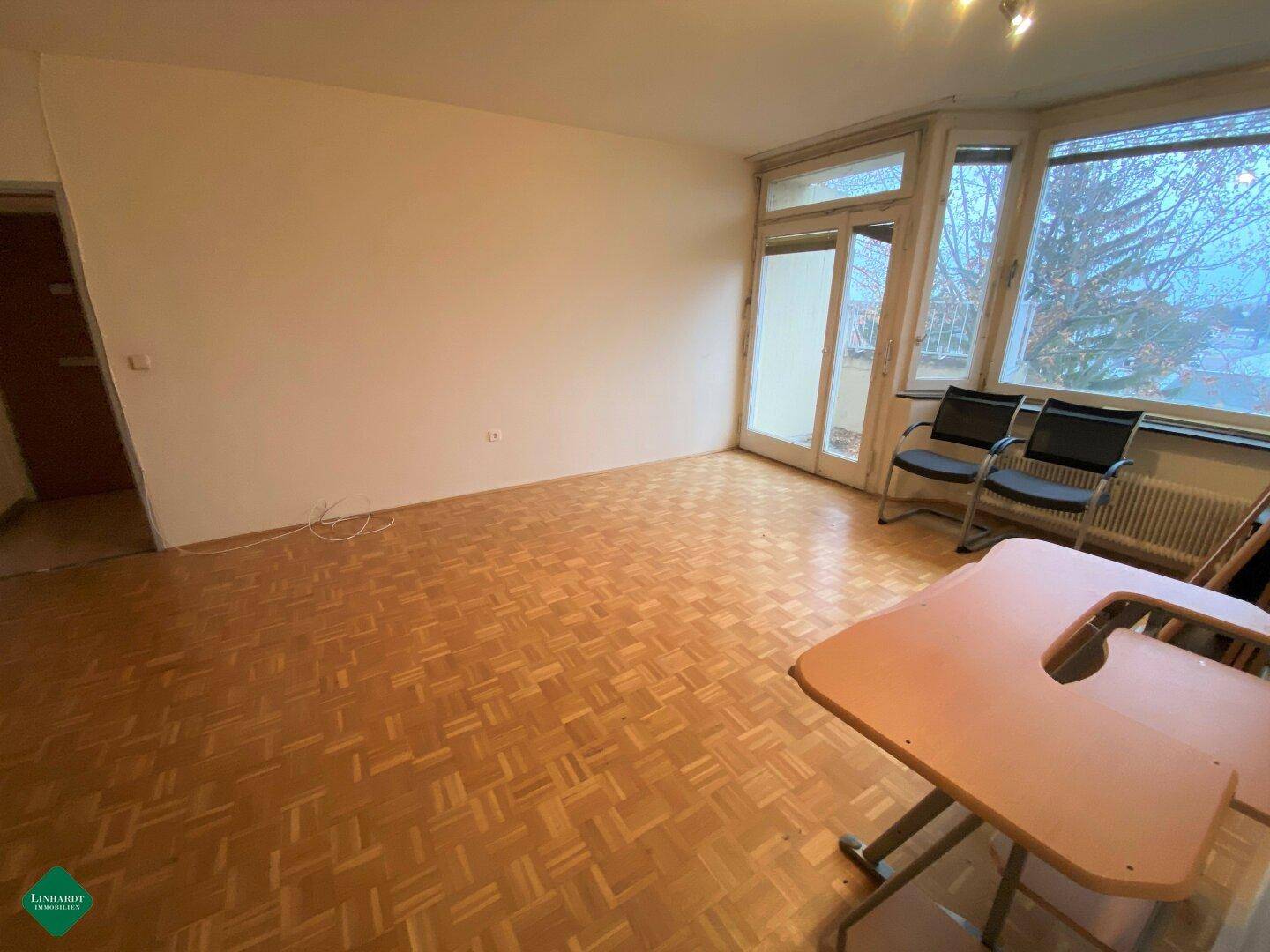 Heller Wohnbereich mit Parkettboden und großen Fenstern, die viel Tageslicht hereinlassen.