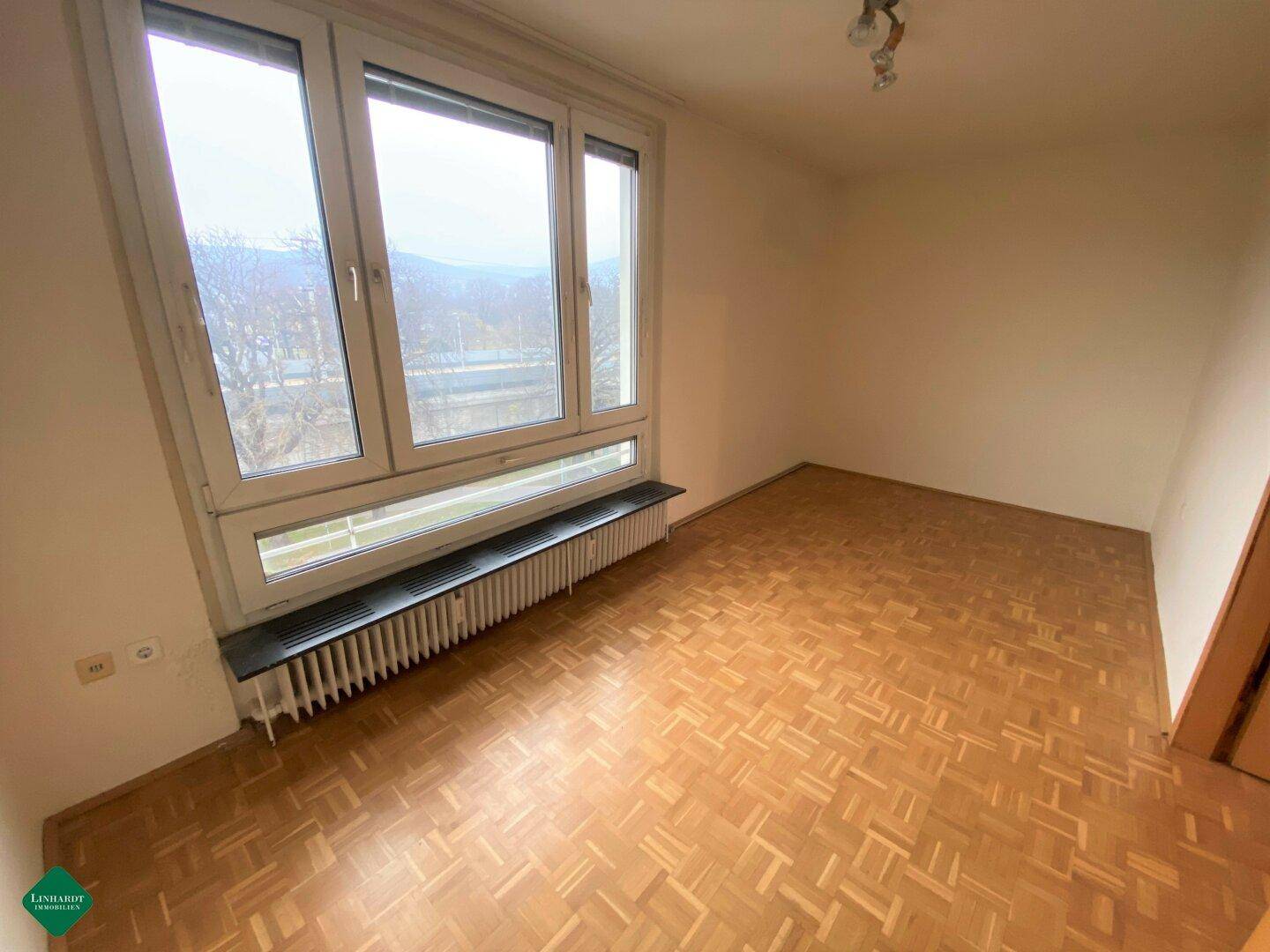 Helles Zimmer mit Parkettboden und großem Fenster, das einen weiten Blick bietet.