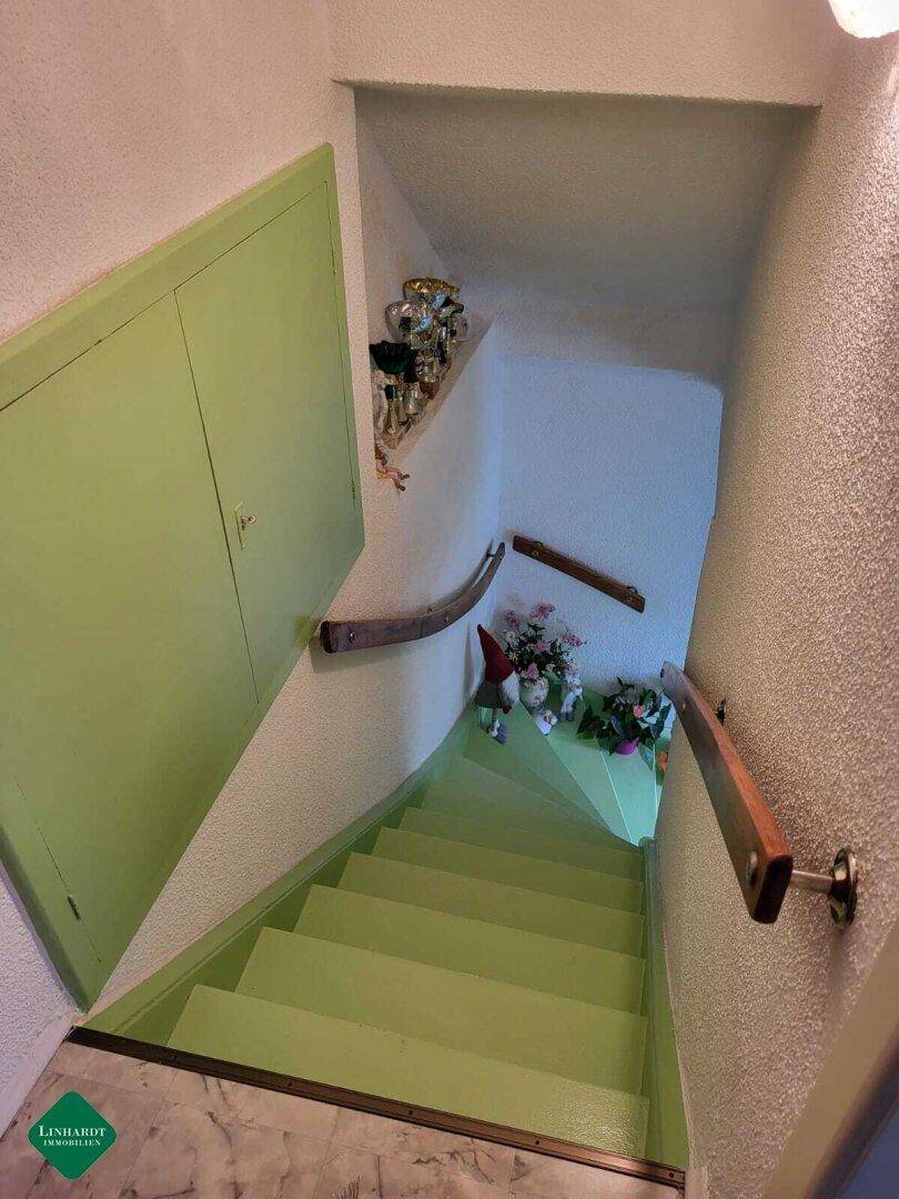 Treppenhaus mit grün gestrichenen Stufen, Holzgeländer und Stauraum unter der Treppe.